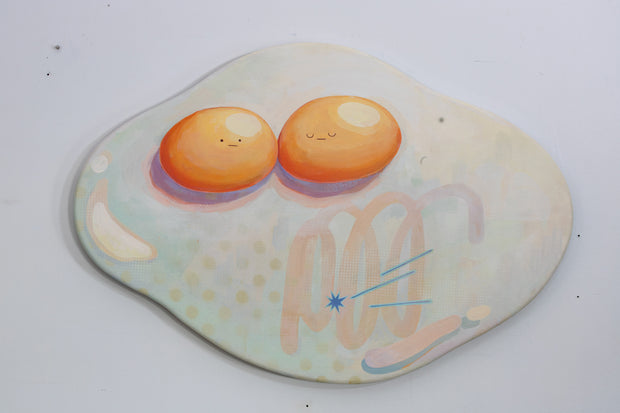 Die cut canvas of a pair of 2 eggs sharing a single egg white. The yolks are touching and have small faces. The egg white contains a subtle polka dot and scribble design.