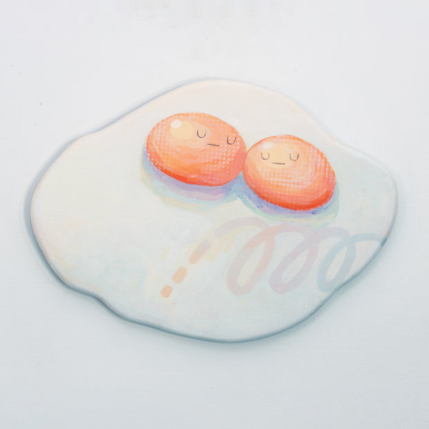 Die cut canvas of a pair of 2 eggs sharing a single egg white. The yolks are touching and have small faces. The egg white contains a subtle polka dot and scribble design.