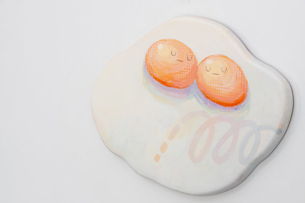 Die cut canvas of a pair of 2 eggs sharing a single egg white. The yolks are touching and have small faces. The egg white contains a subtle polka dot and scribble design.