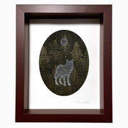 Paper cutting of many yellowish green pine trees, with a silhouette of a wolf painted onto the trees in a light blue. Above, using the same technique is a moon. Framed in a thick wooden frame.