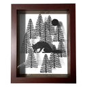 Black paper cutting art of a fox, hunched over and picking up a small star with its mouth. It sheds a small tear and is surrounded by bare pine trees and a full moon. Piece is in thick wooden shadowbox frame.