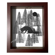 Black paper cutting art of a fox, hunched over and picking up a small star with its mouth. It sheds a small tear and is surrounded by bare pine trees and a full moon. Piece is in thick wooden shadowbox frame.
