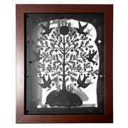 Black paper cutting art of a deer, curled into itself and sleeping. A large tree grows atop of it, with many birds taking star shaped blossoms off the tree. Piece is framed wtih intricate cut paper border. In thick wooden shadowbox frame.