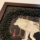 Assembled paper cutting diorama of a large white wolf, following a small girl in a red coat through a forest. They are framed by many cut leaves revealing the scene. Close up showing 3 dimensionality.