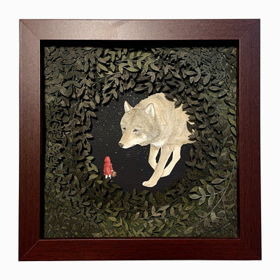 Layered cut paper diorama style sculpture in an open wooden frame, with many layers of leaves revealing a small scene of a red cloaked child facing a very large wolf, which looks at the child.