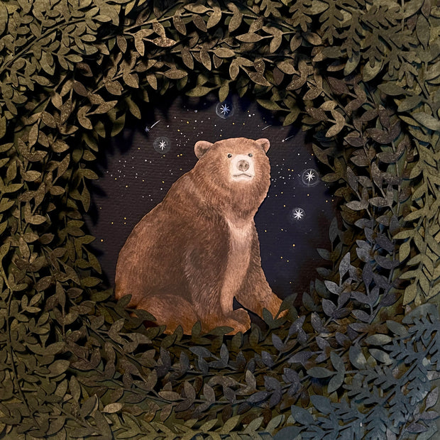 Layered cut paper diorama style sculpture, with many layers of leaves revealing a small scene of a bear sitting and smiling slightly. Shooting stars fall behind it.