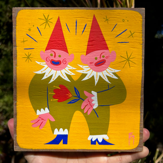 Painting on flat wooden panel with visible grain under the paint. A pair of conjoined cartoon twins wear a single green jumpsuit and pointy hats. One holds a red flower.