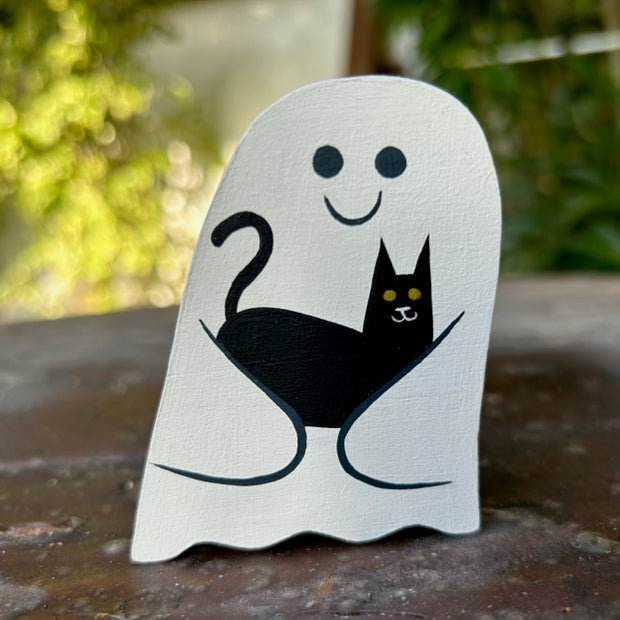 Die cut wooden sculpture of a white, smiling ghost holding a black cat in its arms.