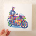 Ink and watercolor illustration of a robot person sitting on a very decorated motorcycle, mostly green and purple with flames, robot decals and text that reads "Giant Robot." The character is dressed mostly in colorful dirtbike attire aside from a black t-shirt and reads an issue of Giant Robot.