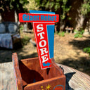 Painted wooden showcase box that holds a blue wooden robot inside. Exterior reads "Giant Robot" written in stylistic retro font, red blue and white. Wooden robot has a flower on its stomach and holds a yellow flag.