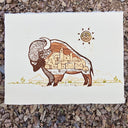 Relief print on paper of a buffalo, with a city inside of its fur and a sun overhead.