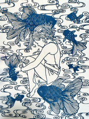 Intricate paper cutting on indigo colored paper of a girl, curled up with her knees drawn in, laying down. Around her are many fish swimming and a swirled water pattern.