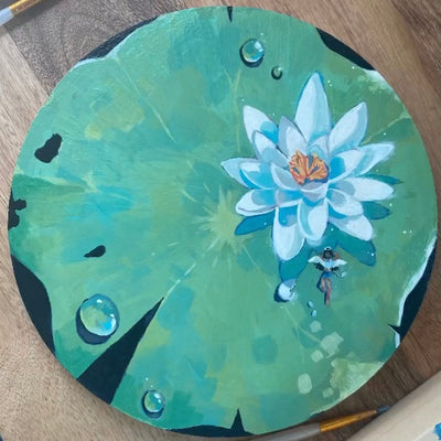 Painting on round wood panel of a large lily pad with a white flower. A small girl with angel wings sits below the flower.