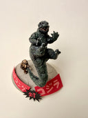 Sculpture of a tiny king kong, throwing around a giant godzilla by his tail on a base with Japanese writing.