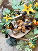 Diorama of a chipmunk eating a piece of pumpkin with a person sitting nearby. They are in an atrium type building made out of sticks with vines growing all around it.