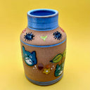 Stoneware vase featuring small, cute illustrations of chibi blue Totoros, holding leaf sprouts with acorns, mushrooms and leaves nearby. Small dust sprites go around the top of the blue lined vase.