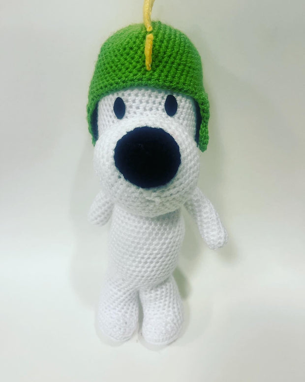 Crocheted sculpture of Snoopy, standing and wearing a knit dinosaur cap, green with yellow spikes.