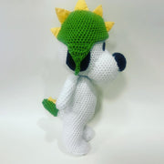 Crocheted sculpture of Snoopy, standing and wearing a knit dinosaur cap, green with yellow spikes.