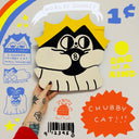 Painted die cut wooden sculpture of a very stylized black and white cartoon cat, holding a magic 8 ball with a bright yellow cartoon sun behind it.