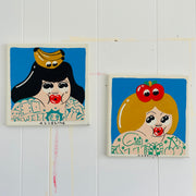 Set of 2 paintings hung on a white wall. Vintage cartoon style woman looking up at fruit atop their head.