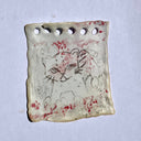 Porcelain sculpture of a sheet of paper with a doodle of a cat on it with red marks, like blood.