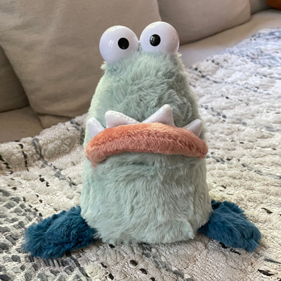 Light green plush of a goofy looking monster creature, with 2 eyes atop its head and a big underbite. It has 3 fins, 2 on each side of its body and one on the back of its tail, like a seal.