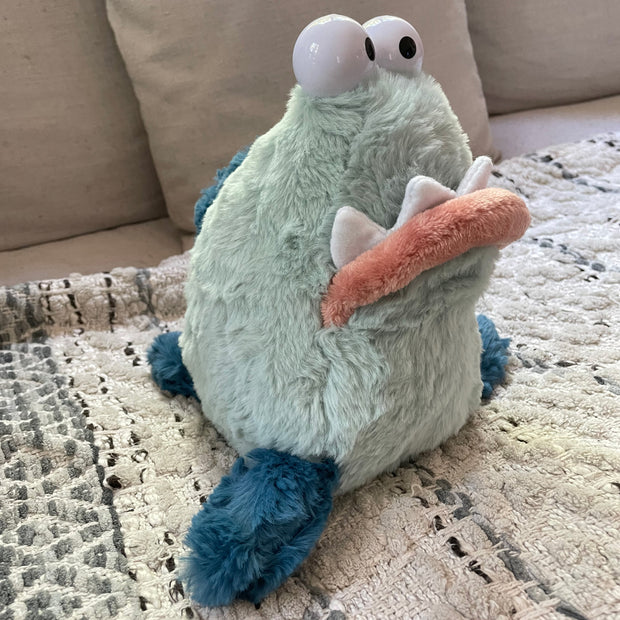 Light green plush of a goofy looking monster creature, with 2 eyes atop its head and a big underbite. It has 3 fins, 2 on each side of its body and one on the back of its tail, like a seal.