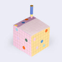 Colorful cube-shaped object with a pen sticking out of it on a light gray background