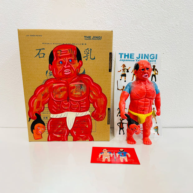 Red soft vinyl figure of a muscular person with black eyes and a sumo wresters loin cloth. It holds a freshly beheaded head in its hands. It stands next to a painted box.