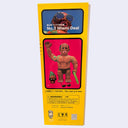Side view of box for Dehara's "Ishida Ho-Nyu" 40cm tall figure, featuring a photograph of the figure - a tan person with many wrinkles on his face, a downturned expression and no eyes. He wears only black underwear and has tattoos.