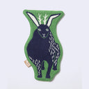 Die cut fabric coaster, shaped to the design of a dark blue jackalope, with a very large, wide body. Border is green.