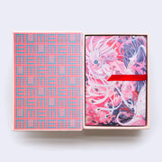Hardcover box of postcards, open to reveal a grid style pattern within the box of "memu" written over and over. A red thread acts as a way to pull out the postcards.