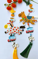 2 hanging with colorful horse clay sculptures, smaller charms including: a tangerine, cup of coffee, car and dog with a yellow tassel on a light blue background