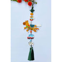 Decorative hanging with a brown horse clay sculpture covered in fruit stickers. Hanging also includes smaller charms: a tangerine, cup of coffee, car and dog with a green tassel on a light blue background