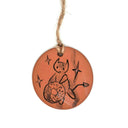 Round terracotta flat ornament with an illustration on it of a cartoon devil and donut design. It hangs from twine.