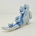 Ceramic sculpture of a Godzilla like kaiju, with rounded edges for its head and arms. Its spikes are rounder, more flower-like shapes.