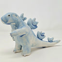 Ceramic sculpture of a Godzilla like kaiju, with rounded edges for its head and arms. Its spikes are rounder, more flower-like shapes.