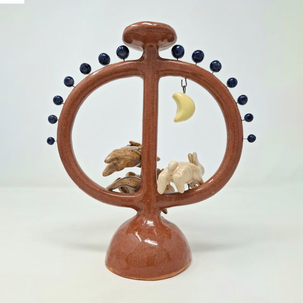 Ceramic sculpture with circular design featuring small rabbits jumping in the middle of the circule and a moon on a white background