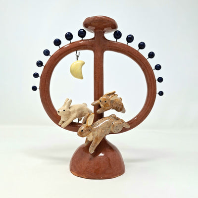 Ceramic sculpture like a candelabra, circular in shape with a support structure running through the middle with rabbits and a moon on a white background