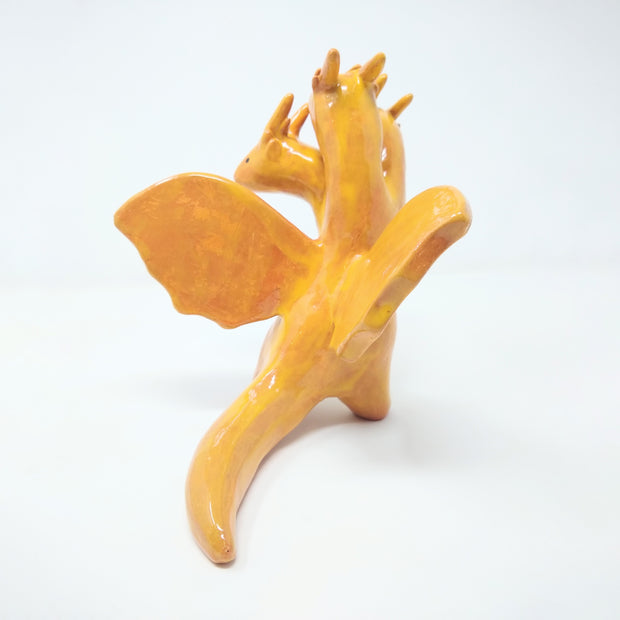 Ceramic sculpture of King Ghidorah, a 3 headed orange dragon monster. It has simplistic body shapes and horns atop its heads. They crane in different directions.