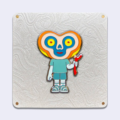 Die cut gold outlined enamel pin of a character with a bean shaped head and the body of a human child. Its eyes are yellow and red and its face is outlined yellow, orange, tan and blue. It holds a red twig and wears striped sneakers.