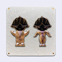 2 die cut gold outlined enamel pins on an elaborate cream color backing card. Both pins are of characters with upside down flowers atop their heads and simple closed eye smiles. Their bodies are abstract in shape and striped gold, with black heads.. 