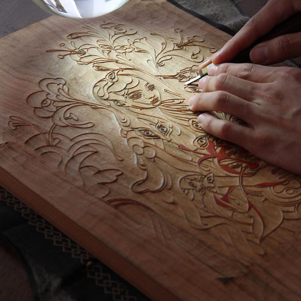 Process photo, showing the artist carving away at a woodblock to reveal the printable image.