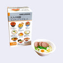 A boxed set of miniature ramen magnets by Kamio Japan Inc. shown next to a small bowl of assembled ramen, on a plain light gray background.