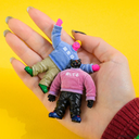 Two small figurines wearing colorful outfits held in a hand against a yellow background