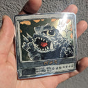 Metallic card with a monster design held in a hand against a textured gray background