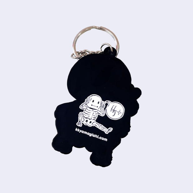 Black keychain with a white skeleton design and website text on a light gray background