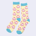 Pair of light yellow socks with blue color accents around the toe, ankle and top. They have a repeating pattern of Kewpie heads, white with a pink outline.