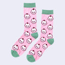 Pair of pink socks with sage green color accents around the toe, ankle and top. They have a repeating pattern of Kewpie heads, white with a burgundy outline.
