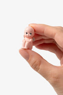 Hand holding a small figurine of a baby against a white background